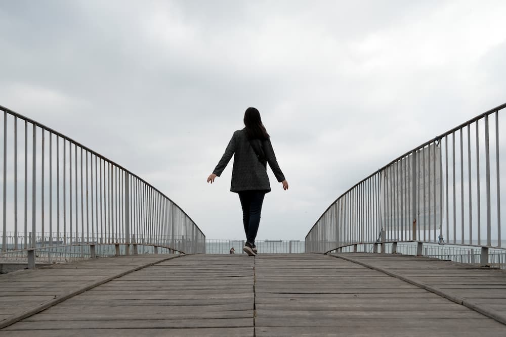 A well dressed woman walks alone down a bridge on an overcast day as Mental Health Services explains how to spend your alone time and not feel lonely